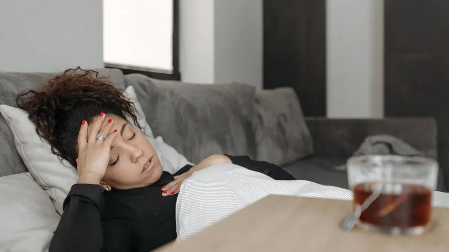 소파에 누워 이마를 짚고 쉬는 사람
